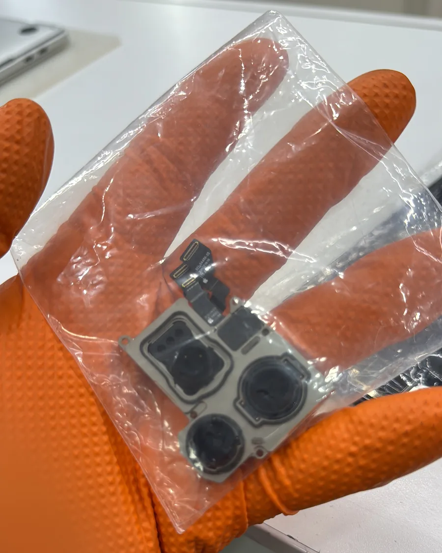 Mano con guante naranja sosteniendo un módulo de cámara triple de iPhone dentro de su bolsa.