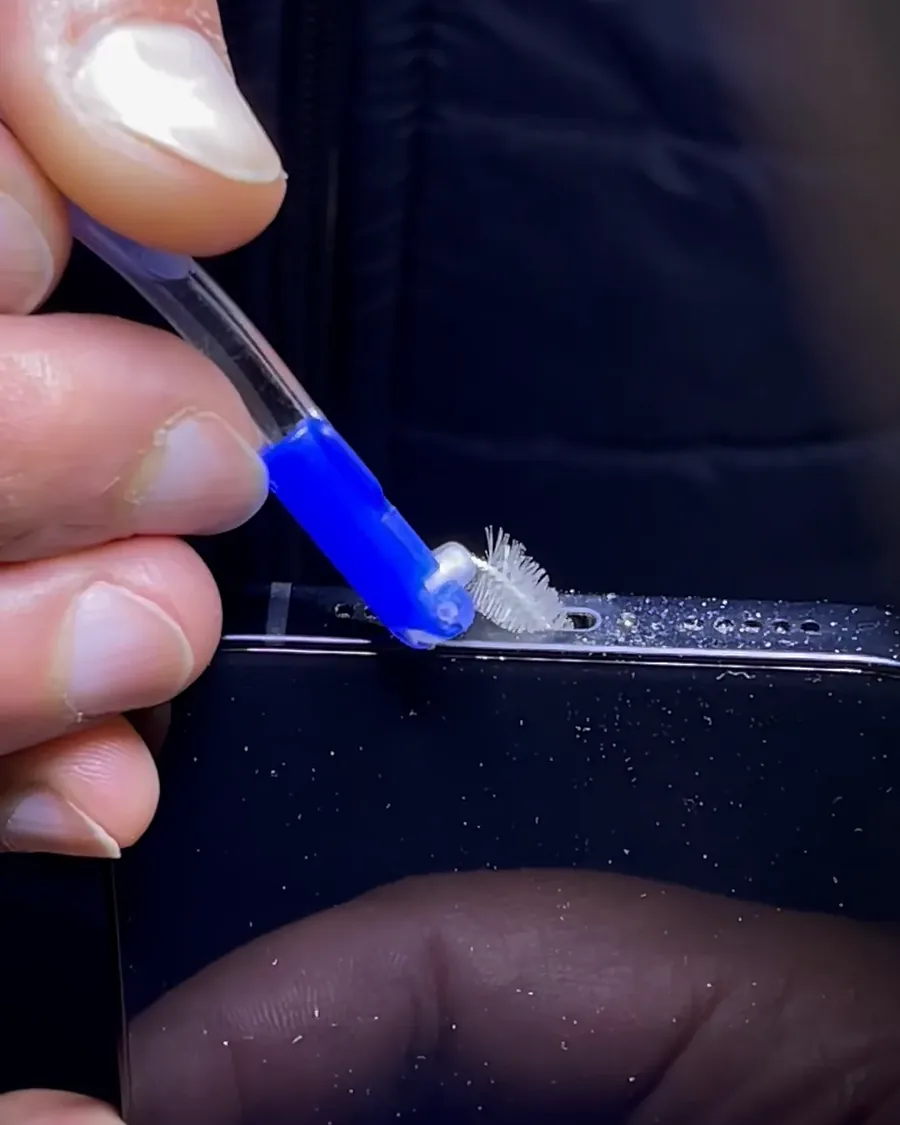 Un cepillo fino limpia el puerto de carga de un iPhone.