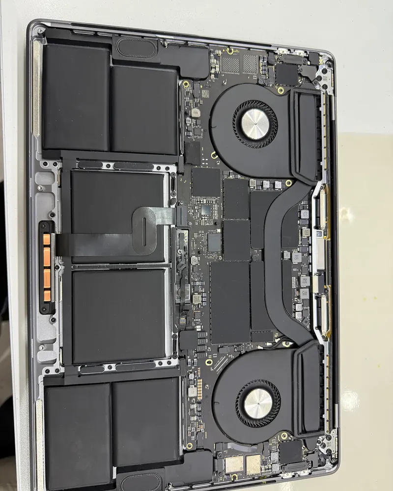 MacBook Pro sin tapa inferior visto desde arriba, con batería, ventiladores y placa a la vista