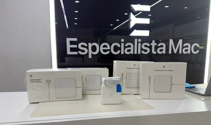Cargadores para MacBook en sus cajas sobre el mostrador, frente al letrero de EspecialistaMac
